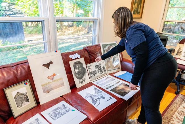 A women arranges art prints on a red couch by a sunny window. The tone is focused and artistic.